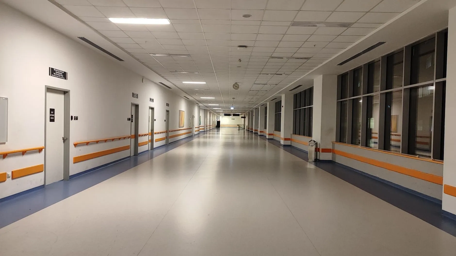 A long, quiet clinic corridor with handrails and closed doors