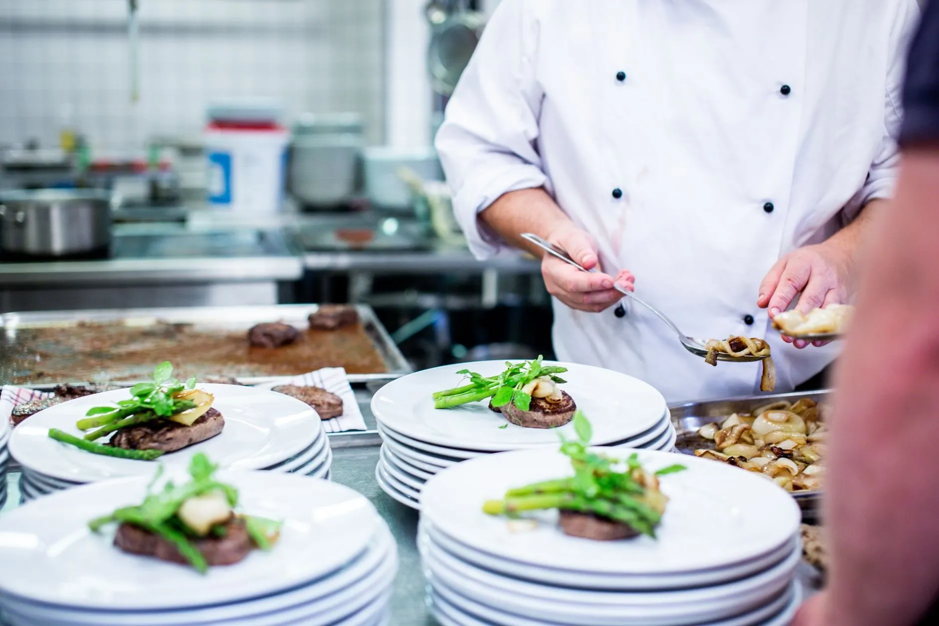 A chef in whites plating a row of dishes at the kitchen pass