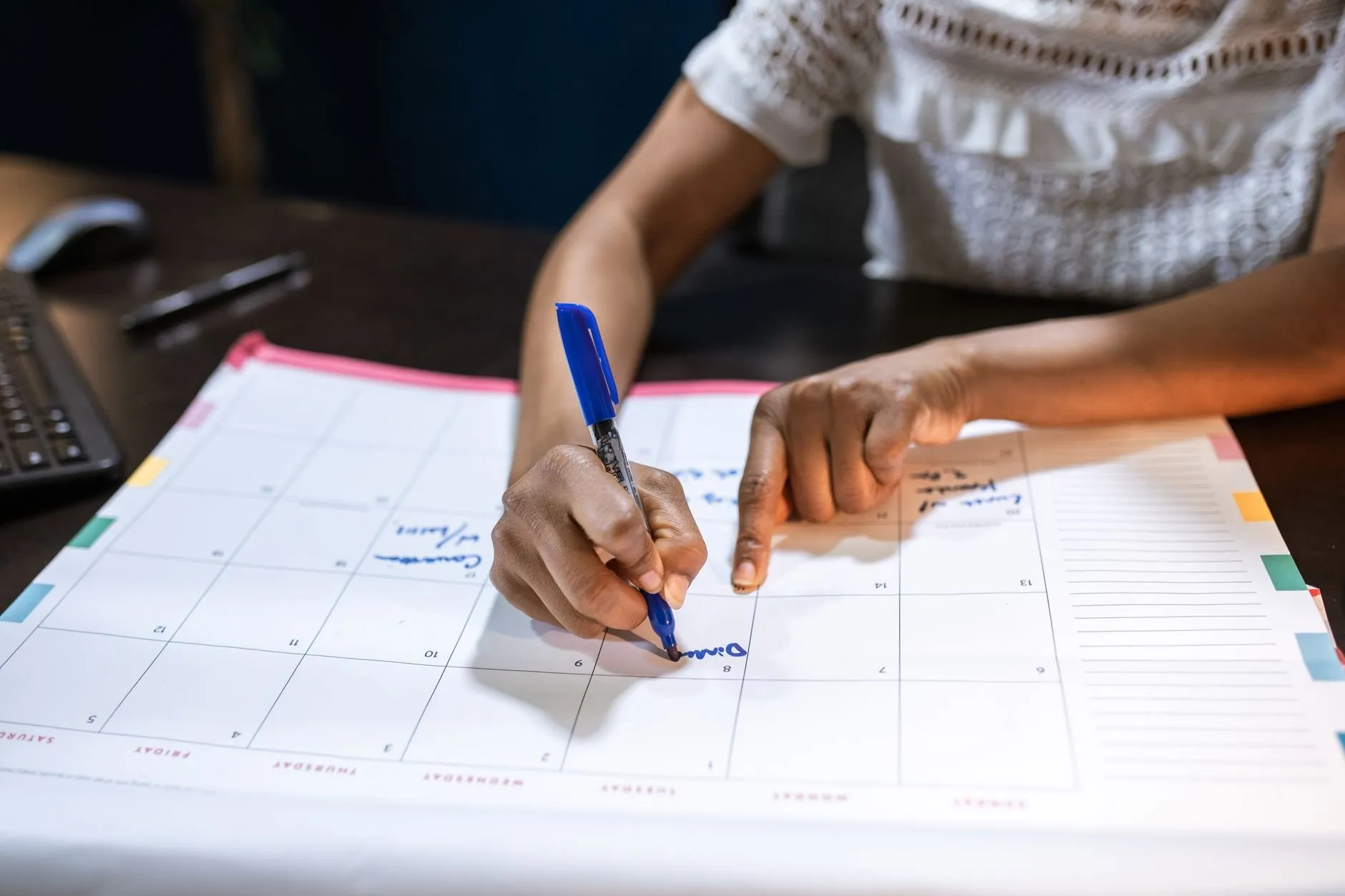 Hands writing shifts onto a large paper wall planner with a blue pen