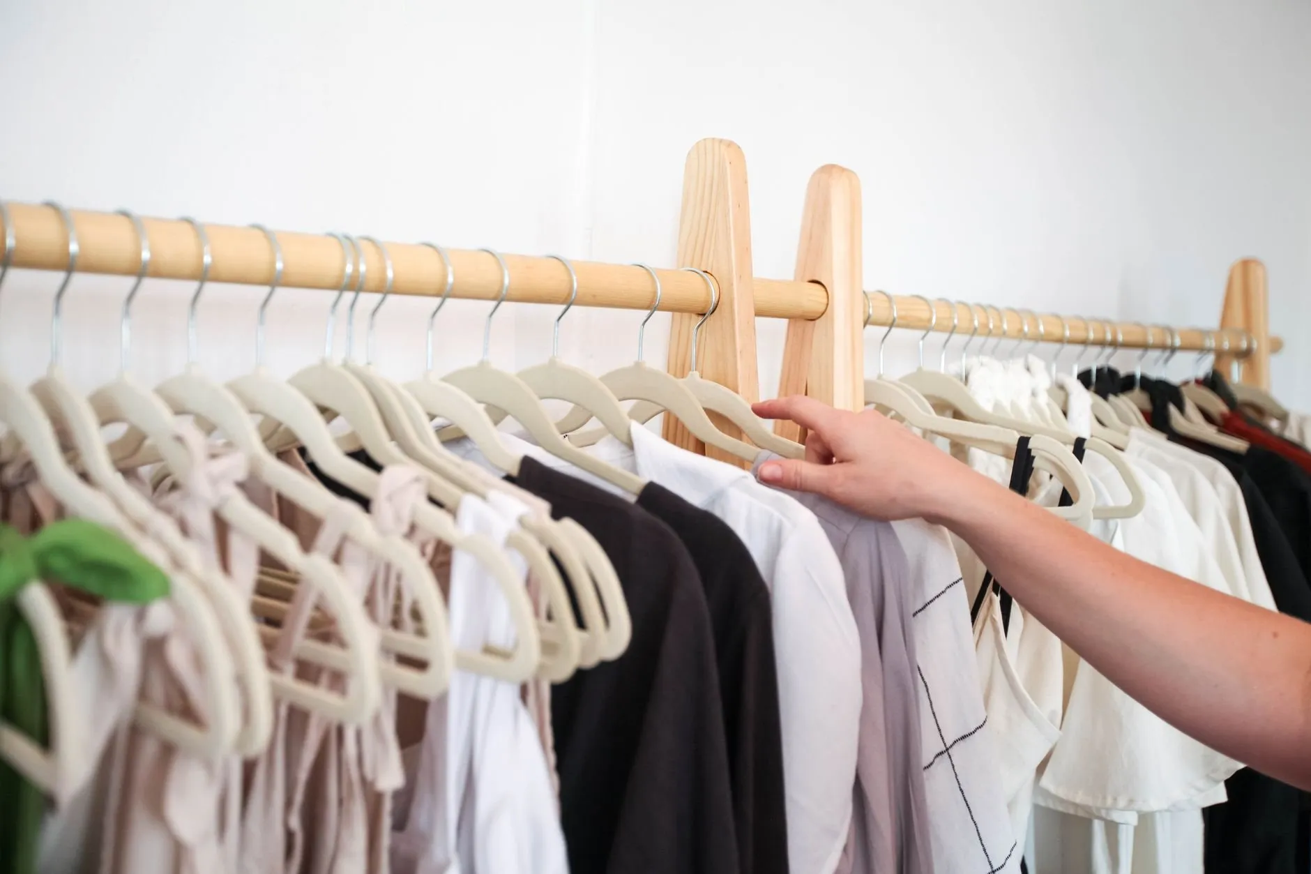 A hand straightening shirts on a wooden clothes rail in a bright shop